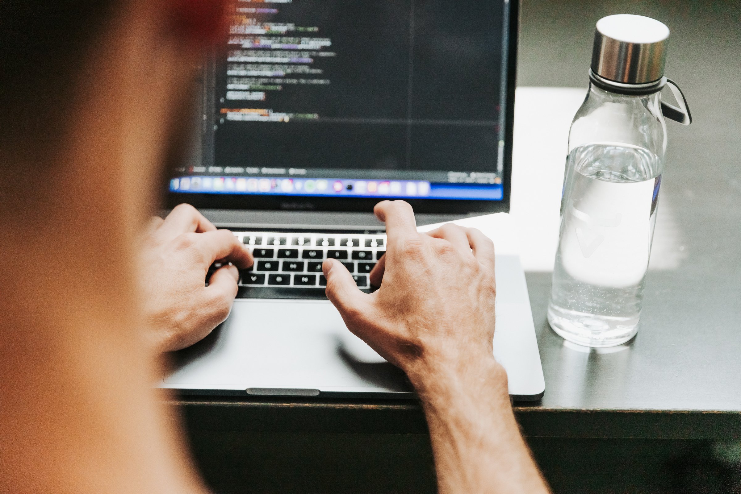 A photo of a developer coding on a laptop, with an IDE visibly open on the screen.