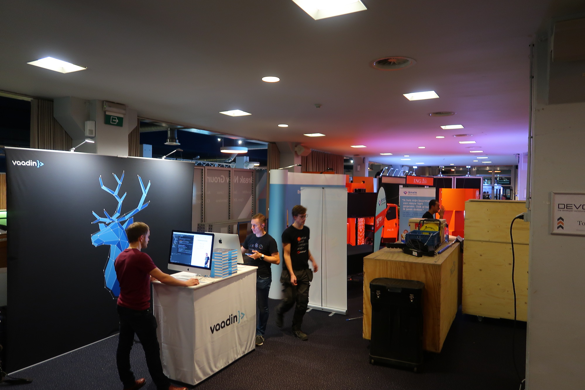 Three men setting up an expo booth with two computers and a stack of books.